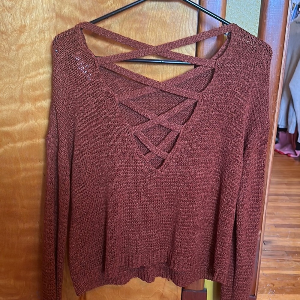 A burnt red knitted sweater, with cross crossing in the back